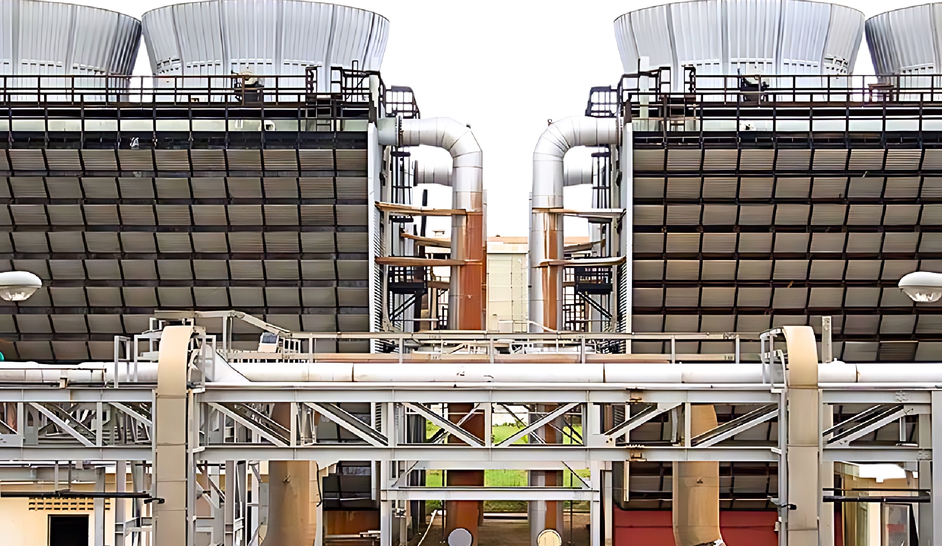 Front view of large industrial cooling towers with multiple ducts, pipelines, and structural frameworks.